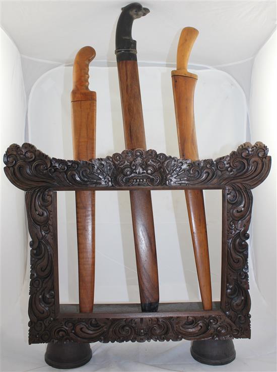 Indonesian carved wood dagger or sword stand, containing three Indonesian or Malaysian swords, early 20th century, longest sword 74(